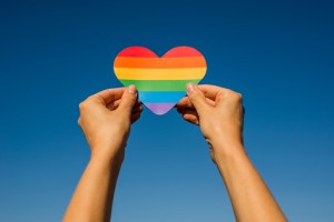 Woman holds in hands a heart in the colors of the rainbow. Young beautiful girl. LGBT history month. Pride Month. Lesbian Gay Bisexual Transgender. LGBT flag. Love, human rights, tolerance. LGBTQ+