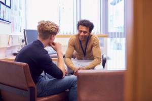 Male College Student Meeting With Campus Counselor Discussing Mental Health Issues