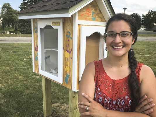 Adriana Flores next to her outdoor cupboard stocked with donated feminine products. Photo courtesy of the Lansing State Journal.